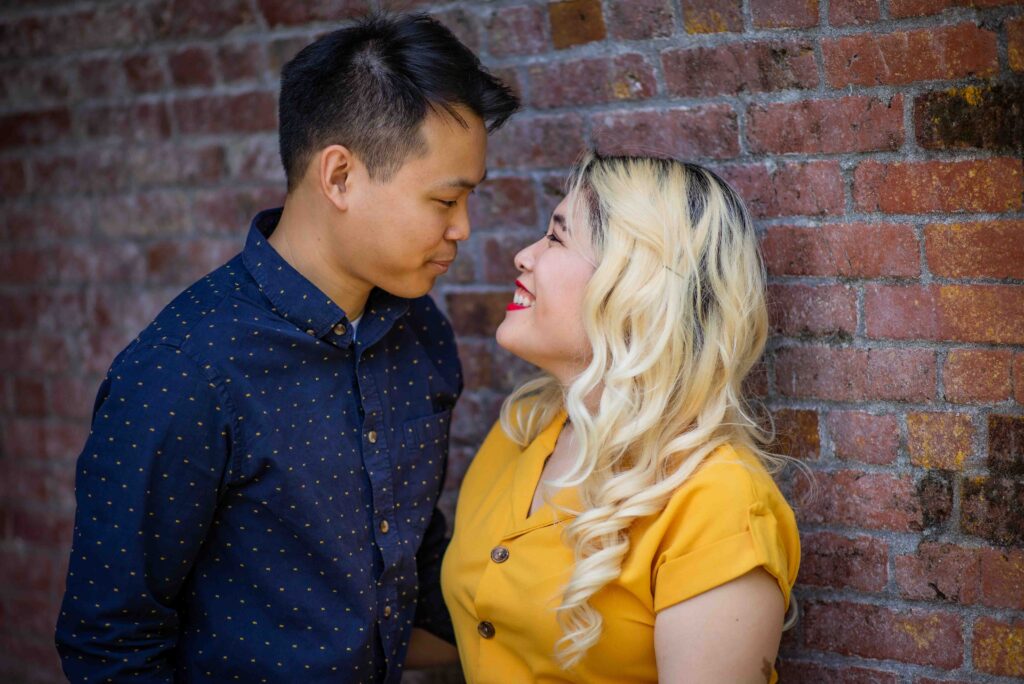 Portrait of an engaged couple staring lovingly at each other in front of some bricks at George Rogers Park in Portland, Oregon.