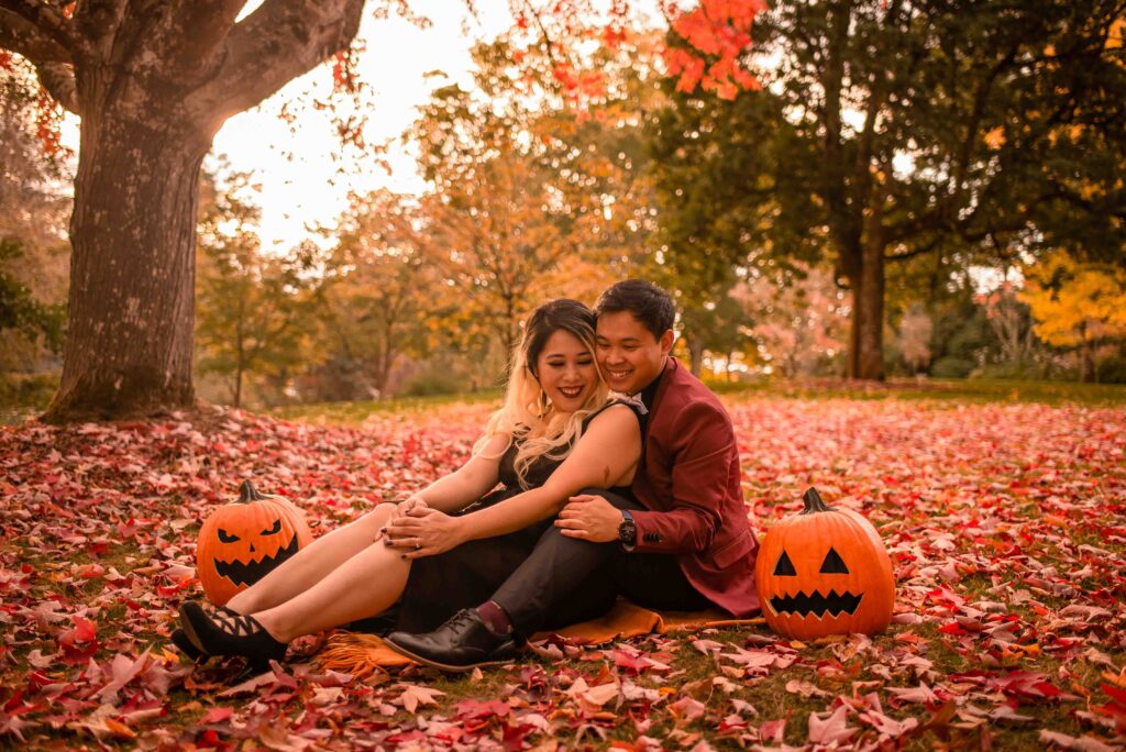 An engaged couples cozies up on a blanket in the fall colors at Bush's Pasture Park in Salem, Oregon. The bright fall leaves and pumpkins set the tone for this fall engagement session.