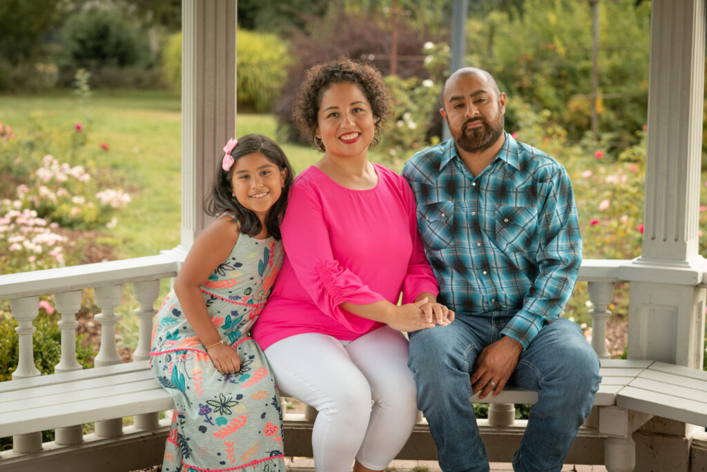 A family photoshoot at Bush's Pasture Park in Salem, Oregon. The family is sitting in the gazebo with the rose gardens blooming behind them.