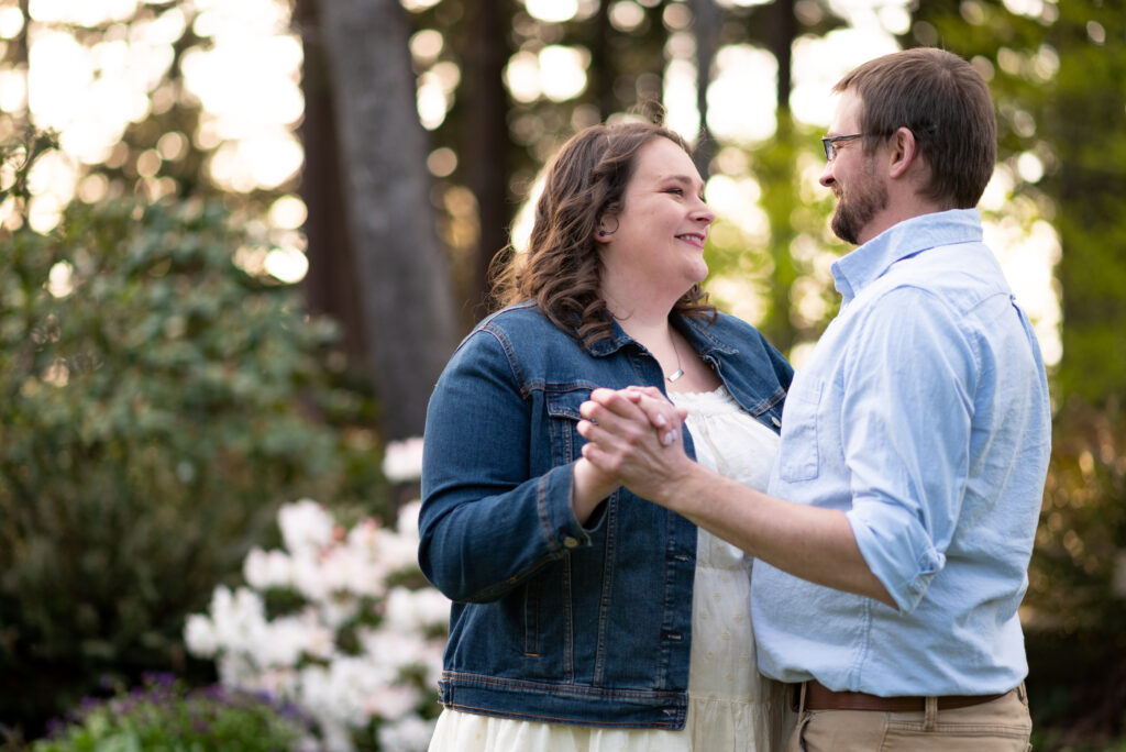 Engagement couple dancing together in the lush greenery of Hendricks Park, Eugene, Oregon, surrounded by blooming rhododendrons.